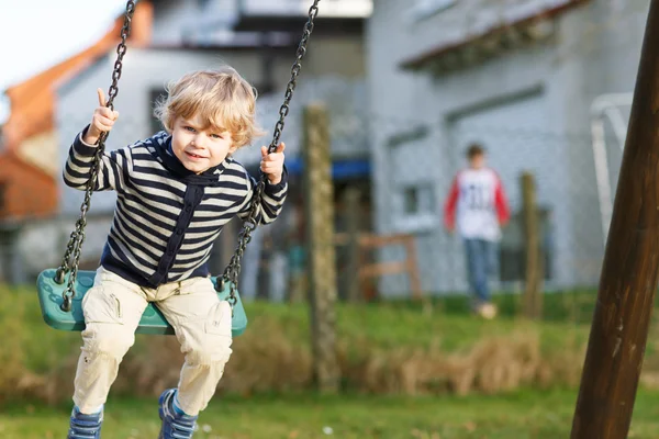 Bedårande barn pojke ha kul kedja swing på utomhus playgroun — Stockfoto