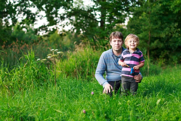 Little boy and his father sitting on grass in summer forest — Zdjęcie stockowe