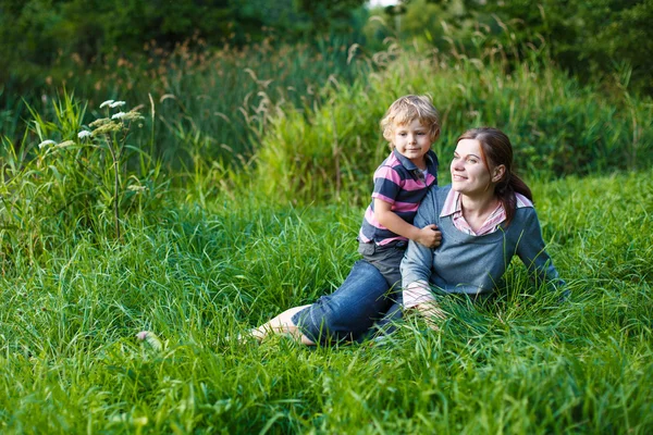 Little boy and his mother sitting on grass in summer forest — Stock Photo, Image