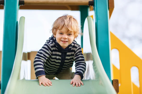 Adorable toddler boy having fun and sliding on outdoor playgroun — Stock Photo, Image