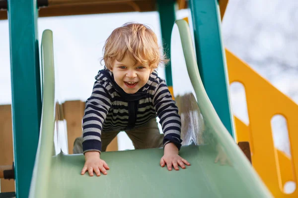 Adorable toddler boy having fun and sliding on outdoor playgroun — Stock Photo, Image