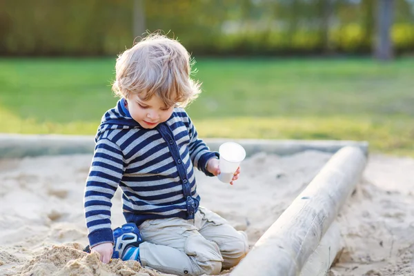 Søte småbarnsgutt som har det gøy med sand på utendørs lekeplass – stockfoto