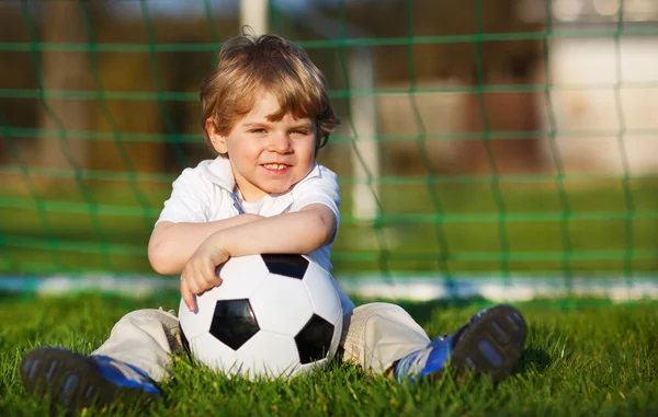 Garçon blond de 3 ans jouant au football avec le football sur le terrain de football — Photo