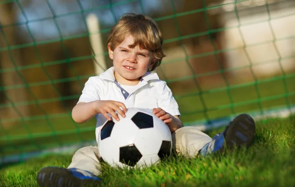 Блондин 3 лет играет в футбол с футболом на футбольном поле — стоковое фото