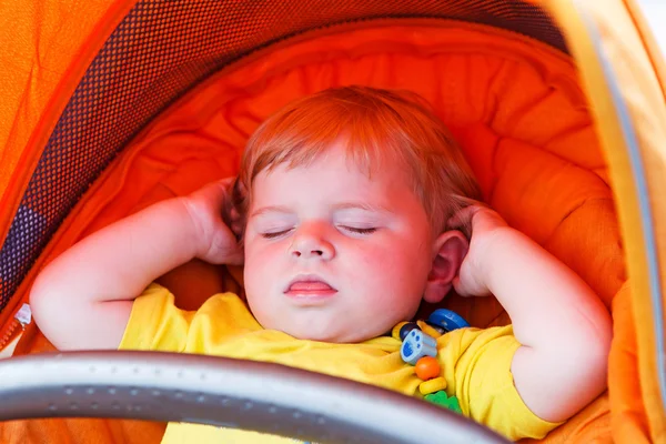 Adorável criança menino dormindo ao ar livre em carrinho de bebê laranja . — Fotografia de Stock