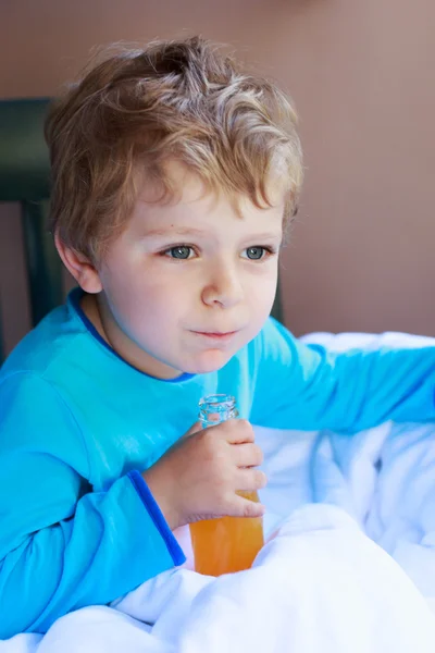 Glücklicher kleiner Junge trinkt Orangensaft nach dem Schlafen, drinnen. — Stockfoto