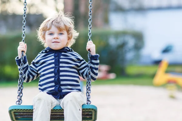 Bedårande barn pojke ha kul kedja swing på utomhus playgroun — Stockfoto