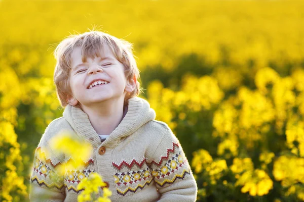 Happy little blond toddler boy lauging in yellow rape field on a — Stock Photo, Image