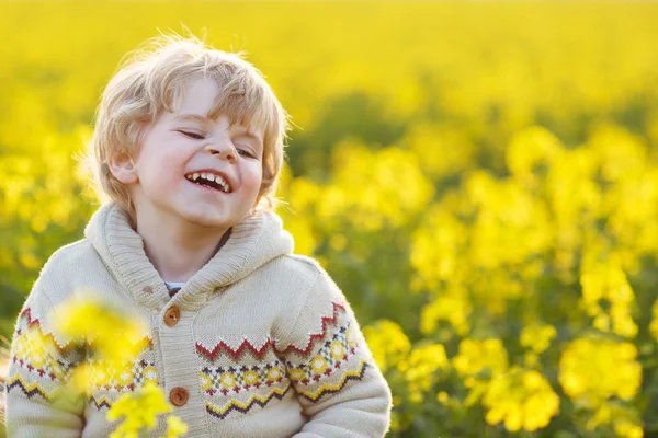 Happy little blond toddler boy lauging in yellow rape field on a — Stock Photo, Image