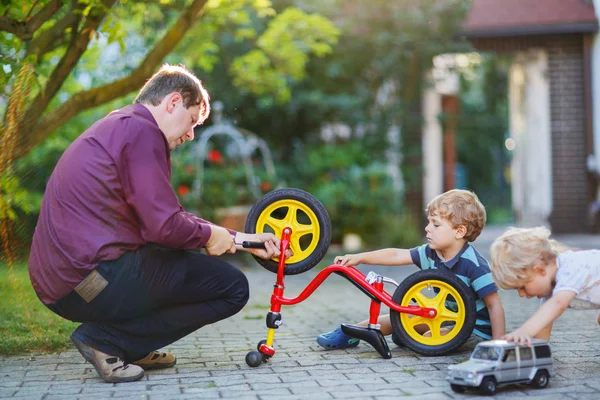 Due fratellini che riparano la ruota della bicicletta con il padre — Foto Stock