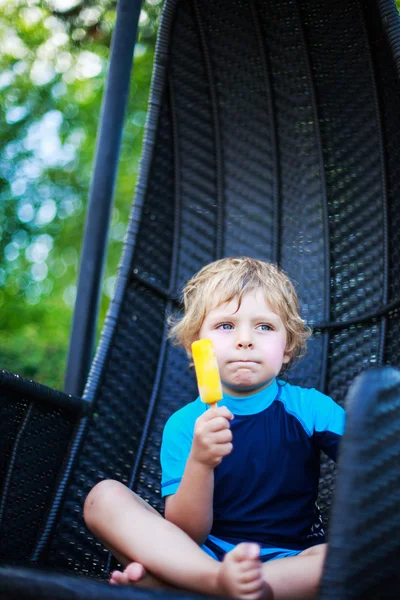 Lindo chico rubio comiendo helado amarillo, al aire libre —  Fotos de Stock