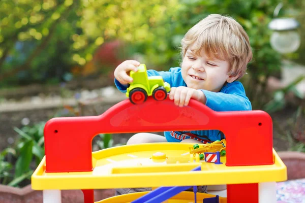 Little blond toddler boy playing with toy - car park station in — Stock Photo, Image