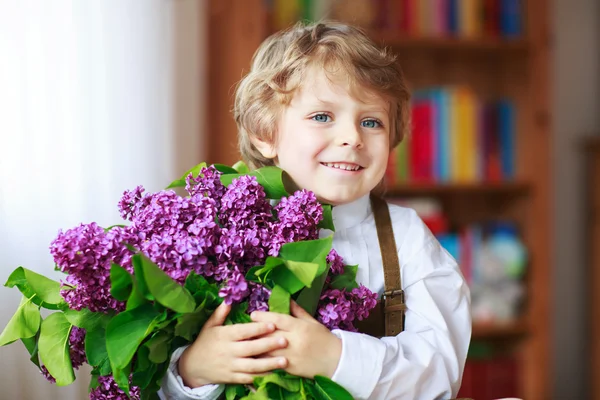 Αξιολάτρευτο χαμογελώντας μικρό αγόρι με ανθισμένα λιλά άνθη — Φωτογραφία Αρχείου