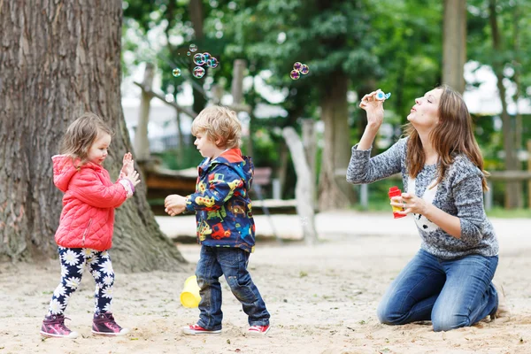 Mor och två små barn som leker tillsammans på lekplats — Stockfoto