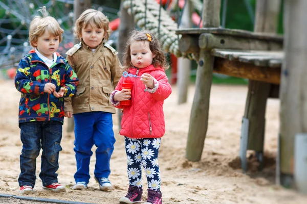 Två små pojkar och en flicka som leker med såpbubblor — Stockfoto