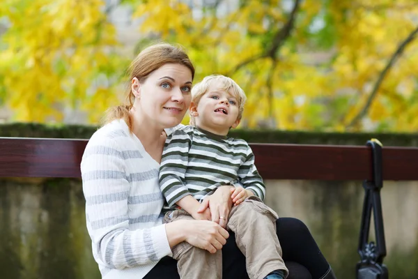 Mother and son sitting on bench in autumn park — Stock Photo, Image