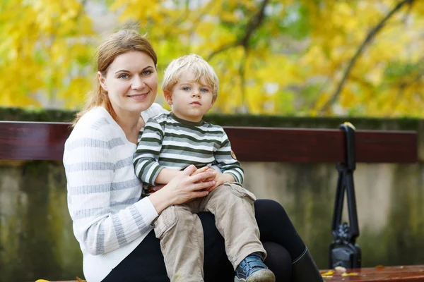 Anne ve oğlu sonbahar parktaki bankta oturmuş — Stok fotoğraf