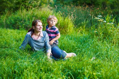 küçük çocuk ve annesi yaz orman çim üzerinde oturan