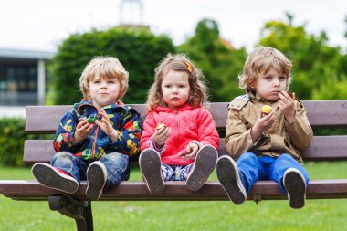 drie broers en zussen zittend op een bankje en het eten van chocolade.