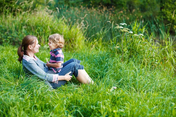 Niño y su madre sentados en la hierba en el bosque de verano —  Fotos de Stock