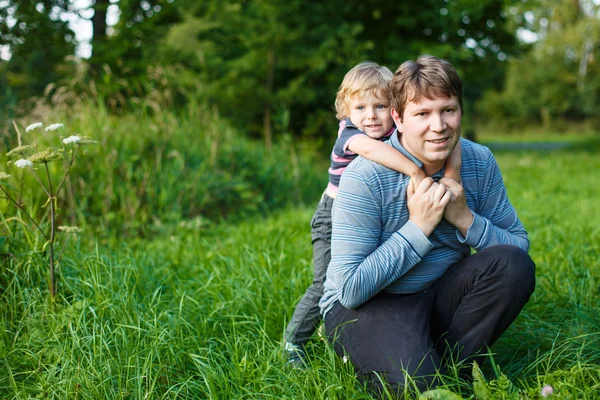 Bambino e suo padre seduti sull'erba nella foresta estiva — Foto Stock