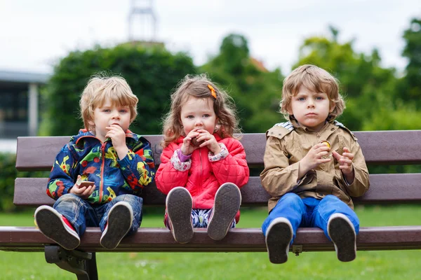 Dos niños pequeños y una niña comiendo chocolate —  Fotos de Stock