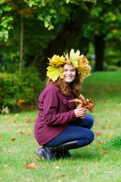 Glückliche junge Frau mit herbstlichem Ahornblätterkranz im Park. — Stockfoto