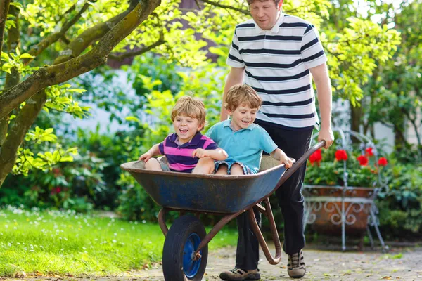 Two little boys having fun in wheelbarrow pushing by father — Stock Photo, Image