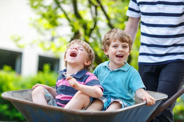 Dois meninos se divertindo no carrinho de mão empurrando pelo pai — Fotografia de Stock