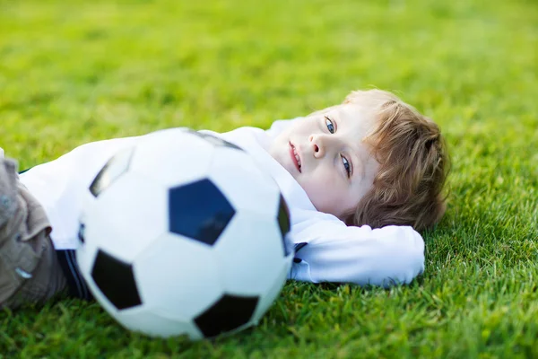 Блондин 4-х лет отдыхает с футболом на футбольном поле — стоковое фото