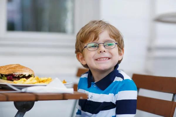 Kleine jongen eten fastfood: Franse frietjes en hamburger — Stockfoto