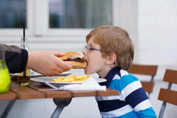 Маленький хлопчик їсть фаст-фуд: картопля фрі та гамбургер — стокове фото