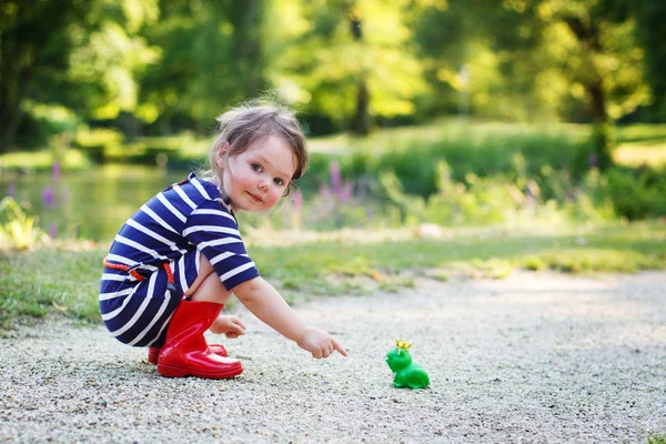 Красива маленька дівчинка в чоботях з червоним дощем грає з гумовою жабою — стокове фото