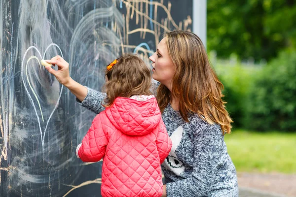 Mãe feliz e filha pequena pintura com giz no parque — Fotografia de Stock