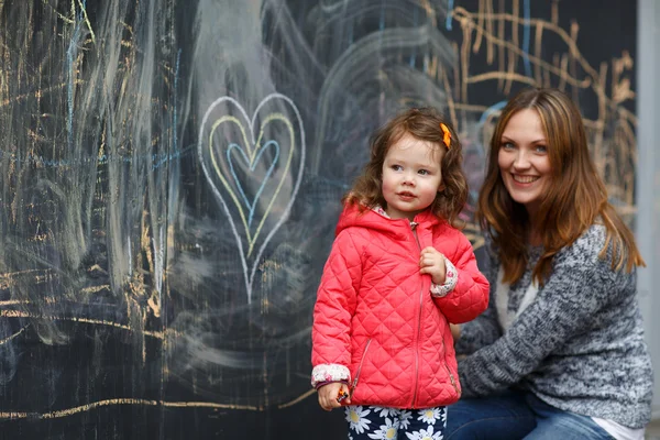 Glad mamma och lilla dotter målning med krita i park — Stockfoto