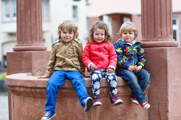 Три брата и сестра сидят вместе на фонтане в городе — стоковое фото