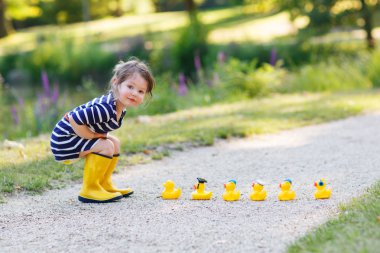 Adorable little girl of 2 playing with yellow rubber ducks in su clipart
