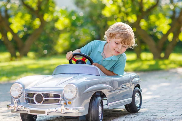 Kleiner Junge fährt großes Spielzeugauto im Freien — Stockfoto