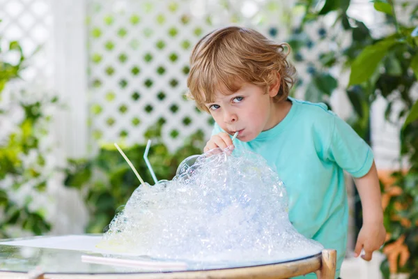 Fröhlicher kleiner Junge experimentiert mit buntem Wasser und Seife — Stockfoto