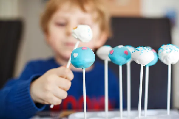 Kleiner blonder Junge isst bunte Cake Pops. — Stockfoto