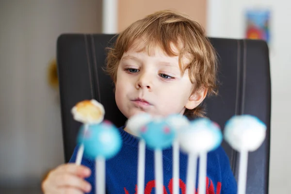 Liten blond pojke äter färgglada cake pops. — Stockfoto