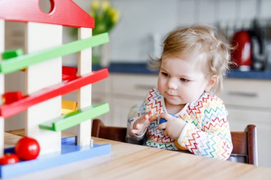 Küçük kız evde ya da çocuk odasında eğitici oyuncaklarla oynuyor. Mutlu sağlıklı çocuk renkli tahta top pisti ile eğleniyor. Çocuk top tutmayı ve yuvarlanmayı öğreniyor. Motorik eğitim.