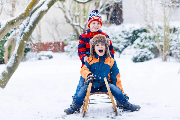 两个小男孩在雪地里玩雪橇游戏.孩子们在雪地上滑行.兄弟姐妹们骑着雪橇。双胞胎在户外玩耍。朋友们在雪地的冬季公园里滑雪橇.家庭假期的积极乐趣 — 图库照片