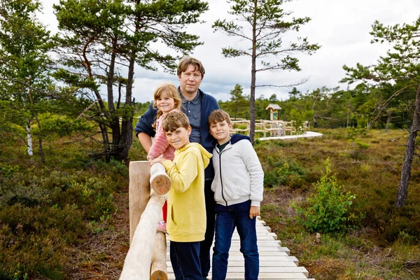 Little girl, two school boys and father walking on wooden path on black moor nature landscape. Active family with three children exploring National Park with trees, plants, boggy landscape. — Stock Photo, Image