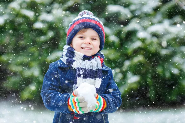 Niedliche kleine lustige Kind in bunten Wintermode Kleidung Spaß haben und spielen mit Schnee, im Freien bei Schneefall. Aktive Freizeitgestaltung im Freien mit Kindern. Junge und Kleinkind fangen Schneeflocken. — Stockfoto