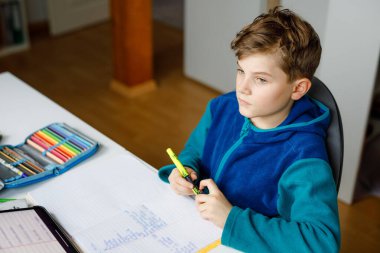 Okul çocuğu evde okul için tabletle öğreniyor. Ev ödevi yapan, ped kullanan ve modern aletler kullanan sevimli bir çocuk. Evde eğitim ve uzaklık öğrenme kavramı.