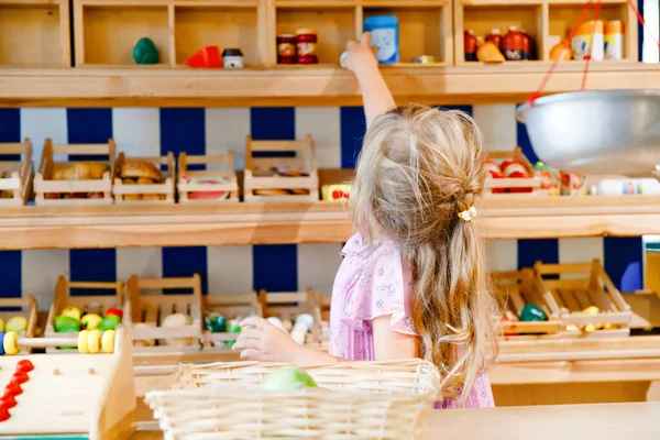 小さな就学前の女の子は食べ物や食料品の木製のおもちゃで遊ぶ。木製の店やスーパーマーケットで、レジや売り手としての役割ゲームを果たして幸せなアクティブ子。教育、子供のための活動. — ストック写真
