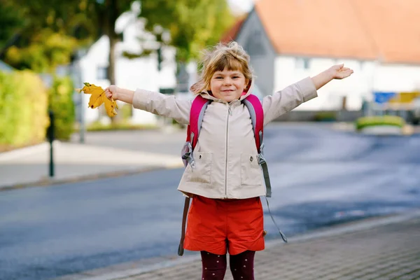 Linda niñita en su primer día yendo a la escuela de juegos. Niño sano y feliz caminando a la guardería. Niño con mochila va a la guardería en la calle de la ciudad, al aire libre —  Fotos de Stock