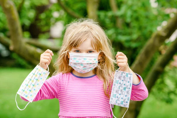 Menina criança em seu primeiro dia a caminho de playschool com máscara médica contra o vírus corona covid. Pré-escolar caminhando para creche pré-escolar e jardim de infância. Criança feliz segurando máscaras — Fotografia de Stock