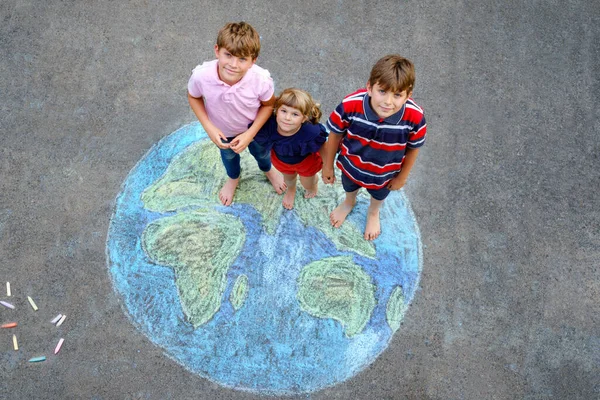 Niña preescolar y dos niños de la escuela con la pintura globo de tierra con tiza de colores en el suelo. Feliz concepto del día de la tierra. Creación de niños para salvar el mundo, el medio ambiente y la ecología. —  Fotos de Stock